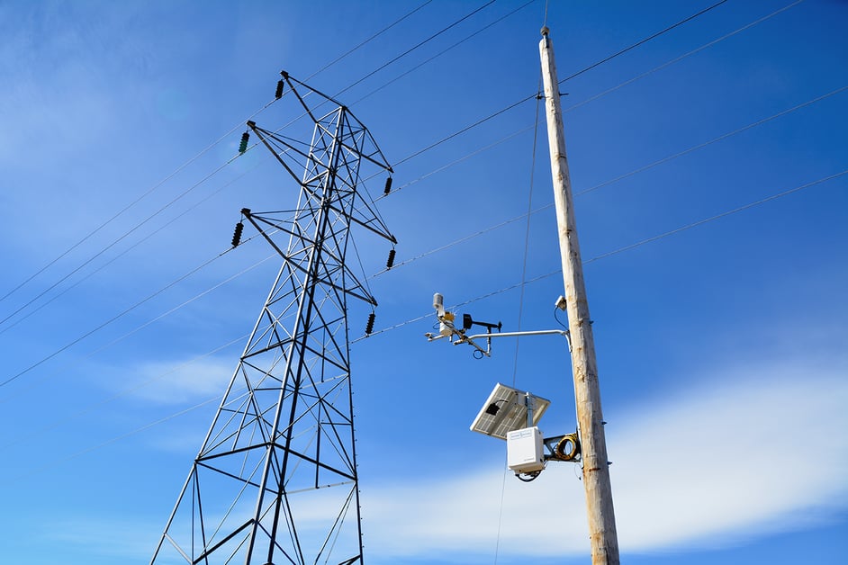 Looking up at an installed Western Weather Group station against a blue sky; mounted to an electric utility pole.