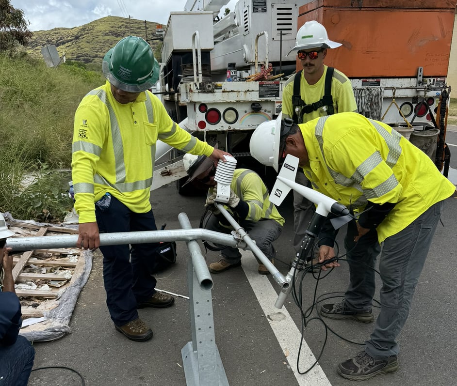 Workers assemble the weather station on the ground before preparing to attach it to a utility pole.