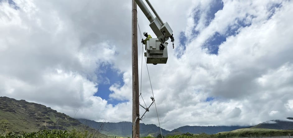 A utility worker hoists up part of the Western Weather Group weather station, starting with the RM Young sensor and several others.