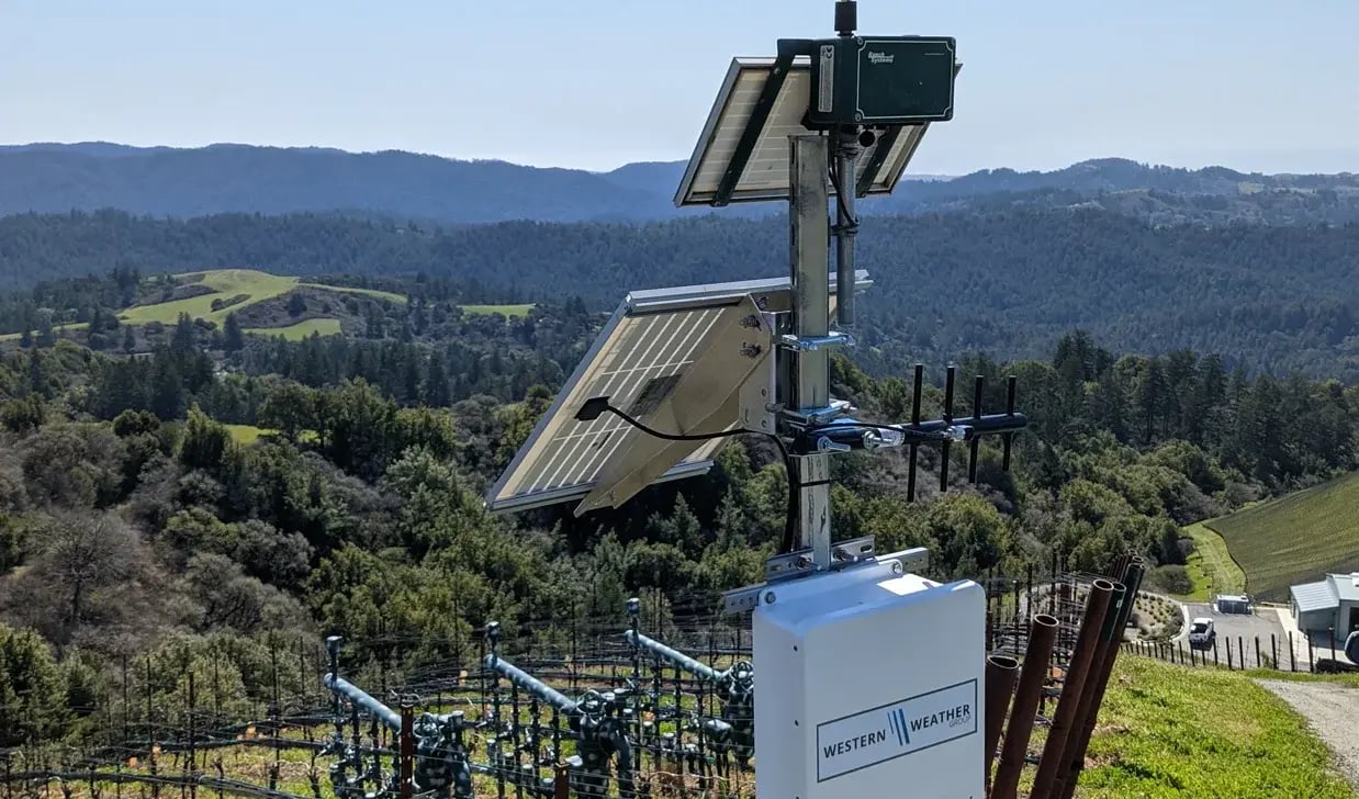 View from behind a weather station looking out onto the crop and landscape below, high on a mountainside.