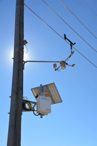 A Western Weather Group weather station mounted on a utility pole against a blue sky.