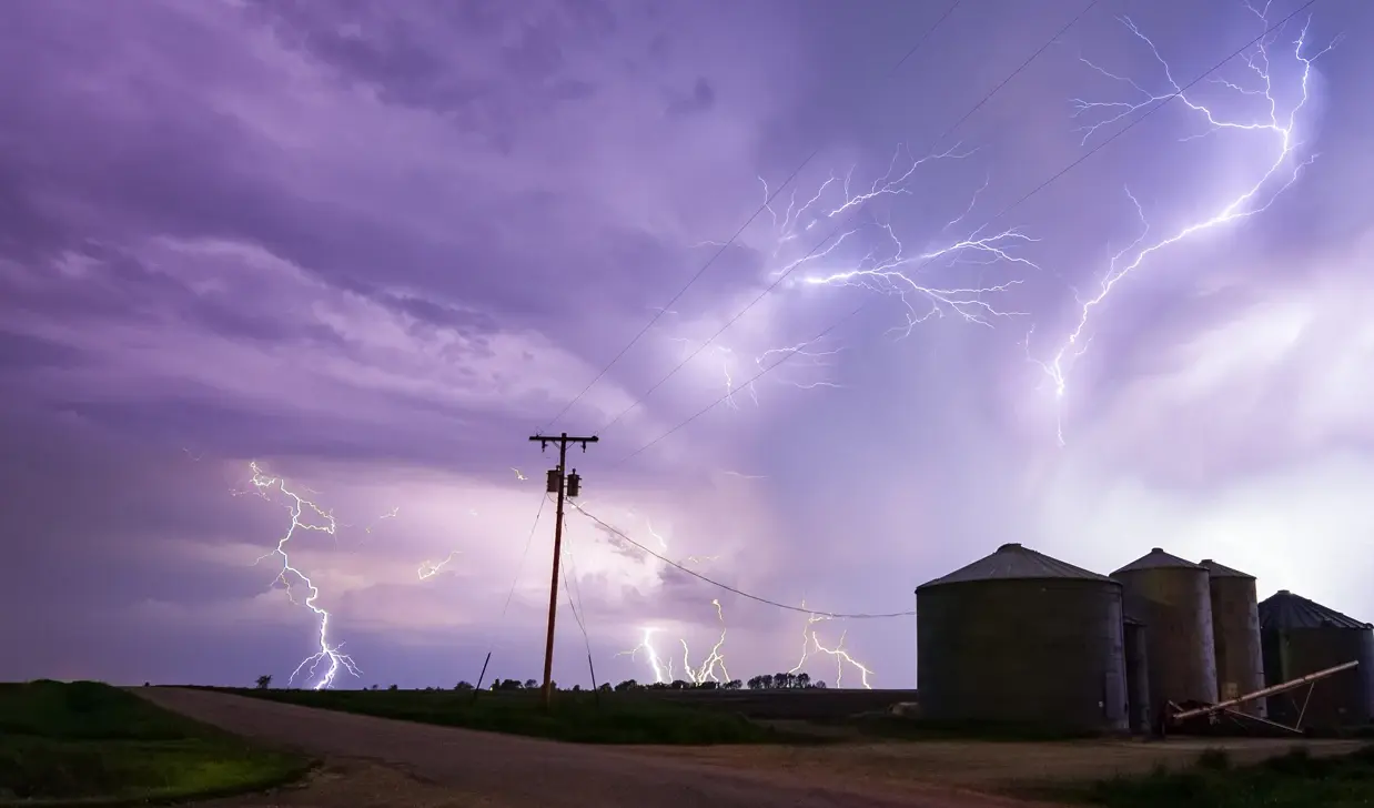 Lightning strikes a farm with utility poles in the foreground